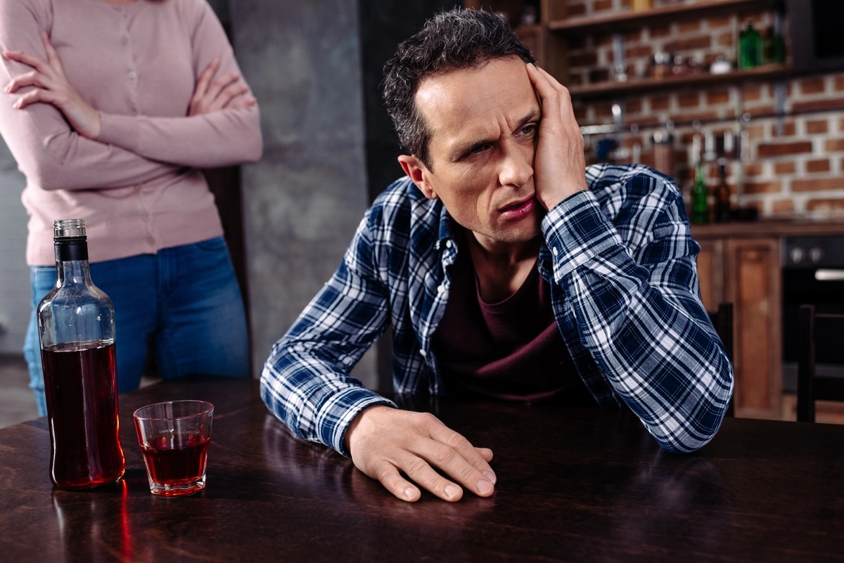 Alcohol Addiction: Man glaring across the room drinking at a table