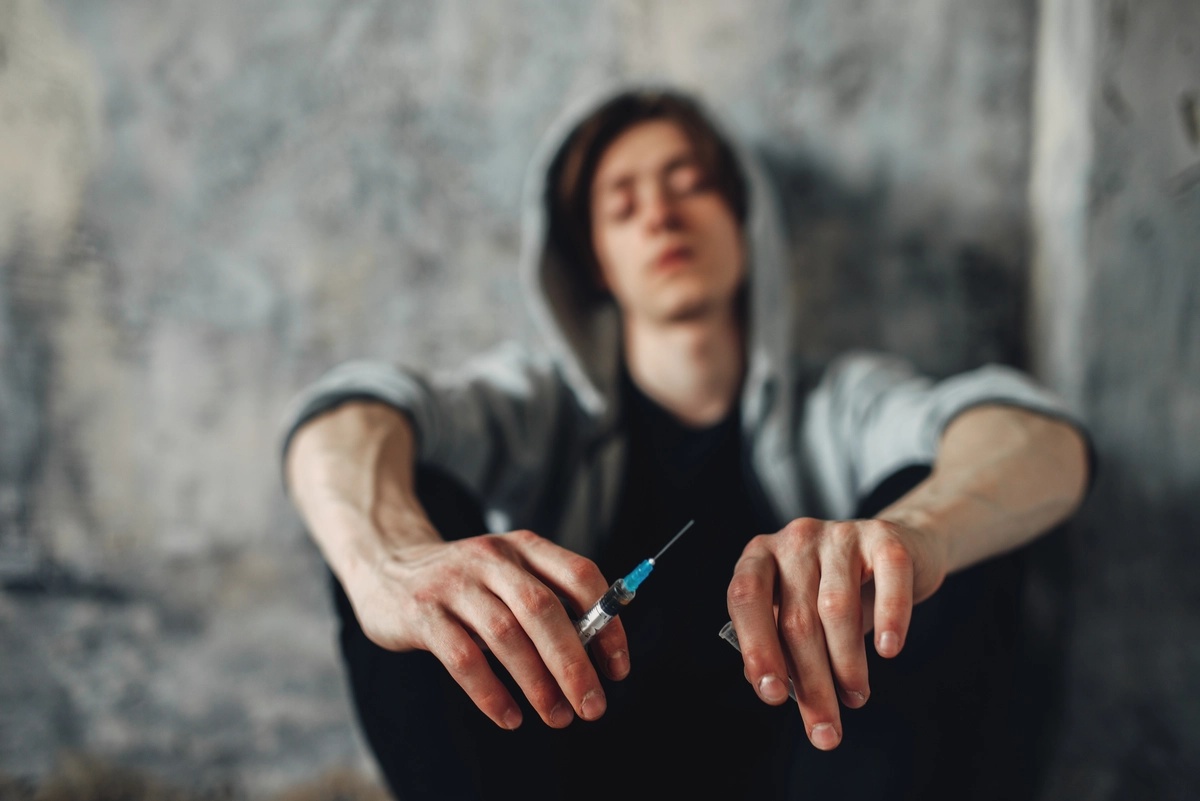 Meth Addiction: Close up shot of man sitting against a wall with a syringe