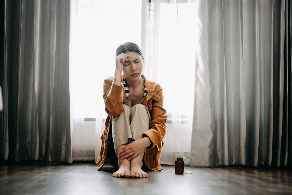 Prescription Drug Addiction: Woman kneeling on the floor with a pill bottle